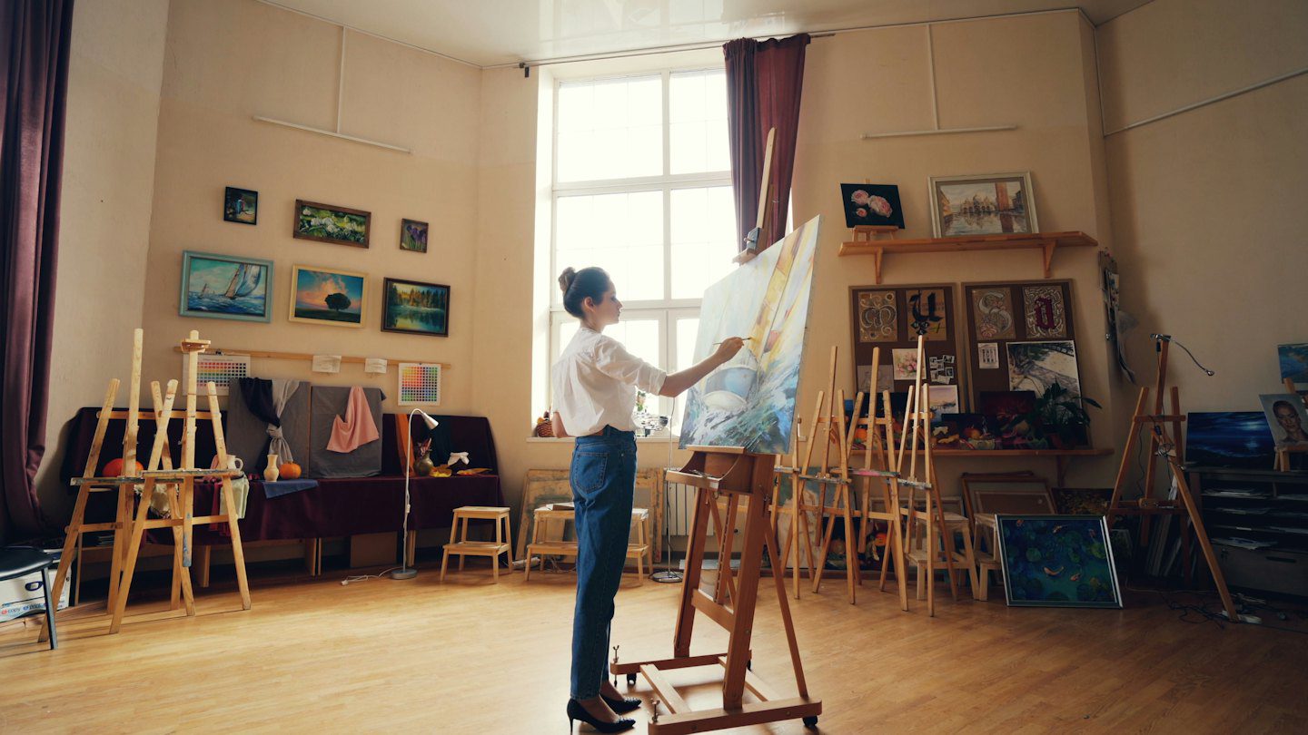 Artista pintando un gran lienzo en un estudio luminoso.